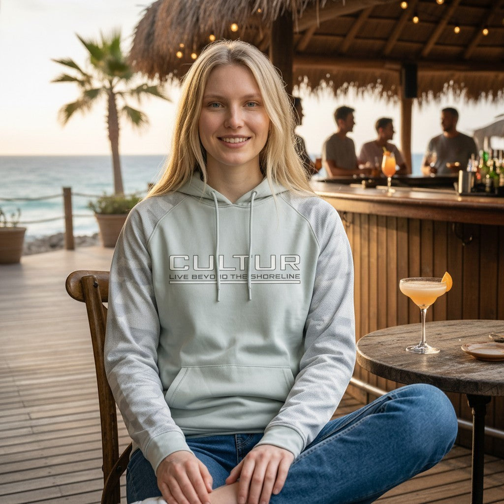 CULTUR aluminum coastal hoodie with minimalist logo and camo sleeve accents worn by a woman sitting outdoors.