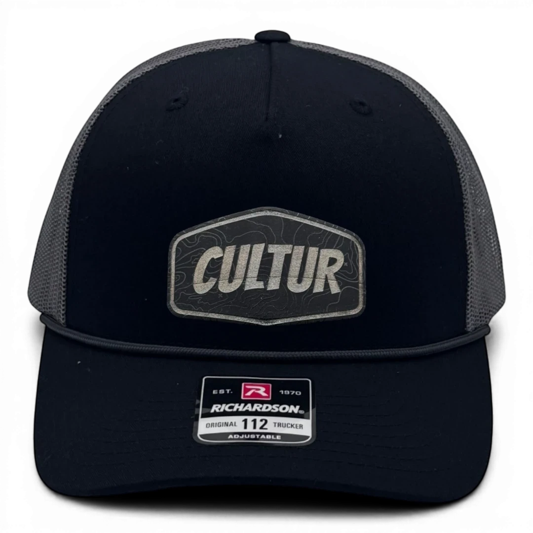 CULTUR black-charcoal trucker hat with grey mesh back and embroidered CULTUR Topo patch. Adjustable.