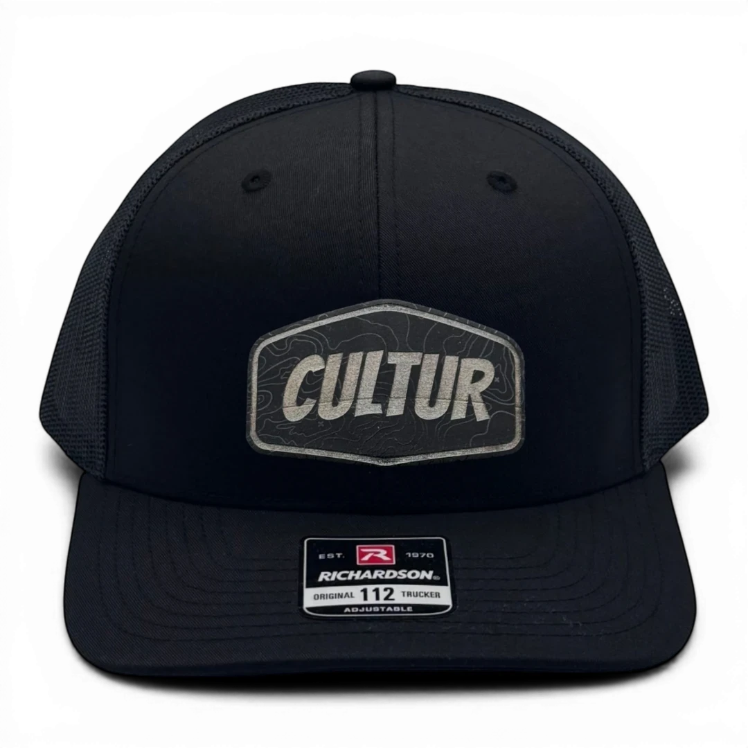 CULTUR black trucker hat with mesh back and embroidered CULTUR Topo patch. Adjustable fit.