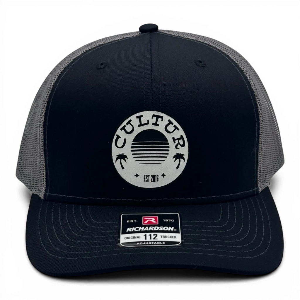 CULTUR black trucker hat with grey mesh back and circular logo featuring palm trees and a sunset design.