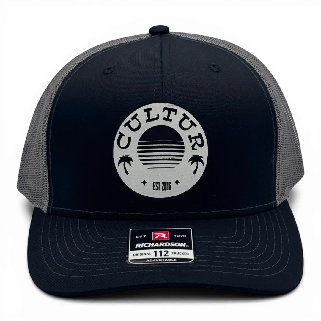 CULTUR black trucker hat with grey mesh back and circular CULTUR logo featuring a sunset and palm trees.