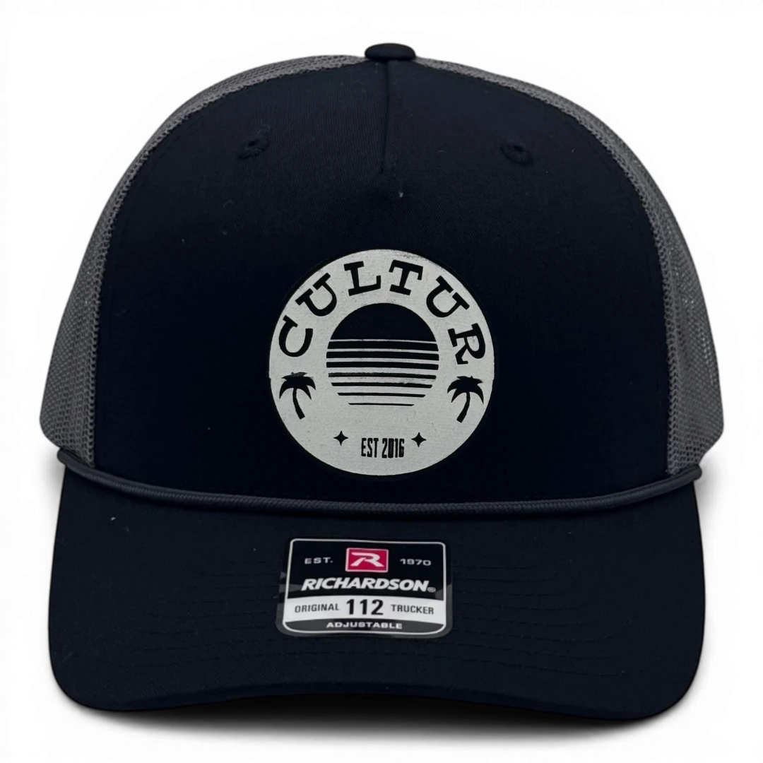 CULTUR black trucker hat with grey mesh back and circular CULTUR patch with sun and palm trees.