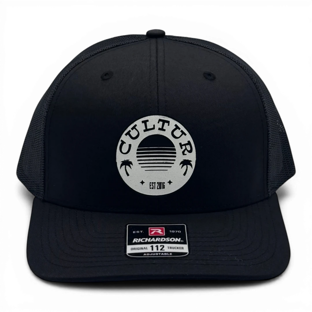 CULTUR black trucker hat with mesh back and circular logo featuring a sunset design with palm trees and "EST 2016".