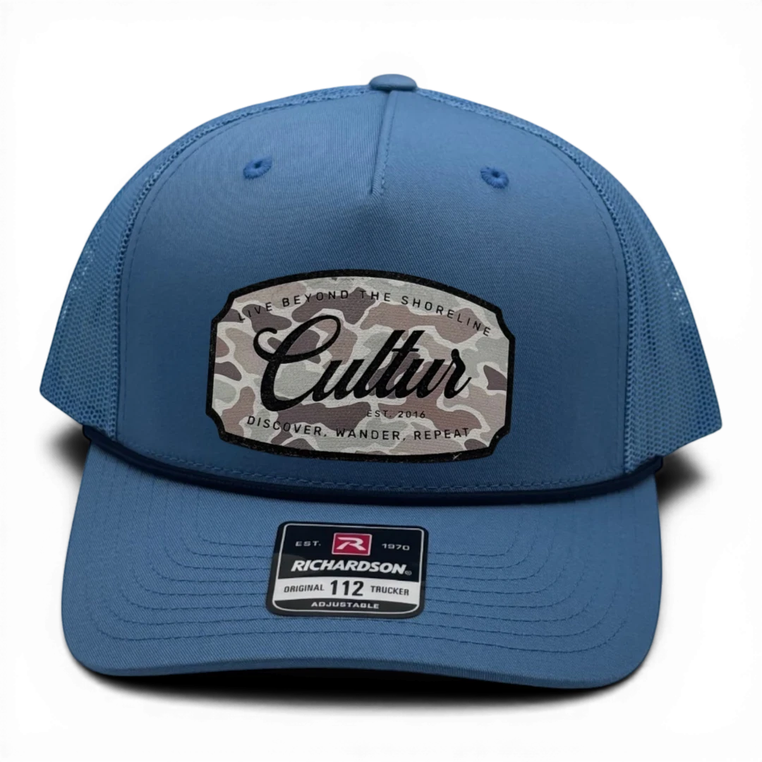 CULTUR blue trucker hat with a camouflage patch featuring the brand name and