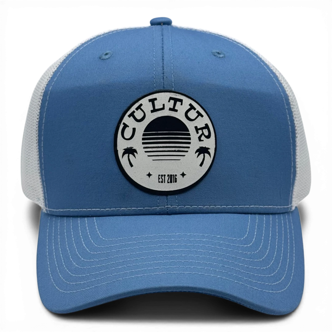 CULTUR blue trucker hat with white mesh back and circular patch featuring palm trees and a sunset design.