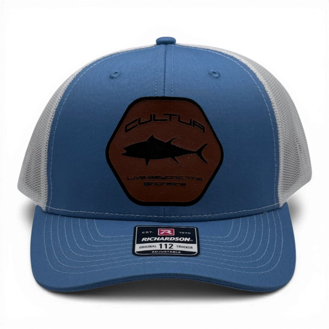 CULTUR blue trucker hat with white mesh back and a hexagonal patch featuring a black tuna silhouette and CULTUR logo.