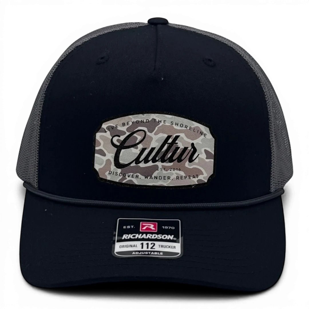 CULTUR black trucker hat with grey mesh back and a camouflage patch featuring the CULTUR logo and text.