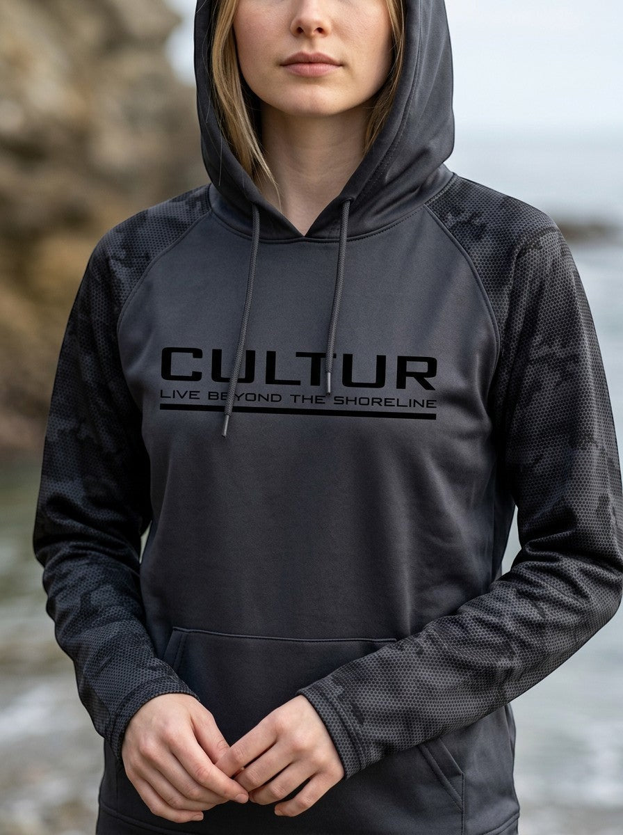 CULTUR graphite grey microfiber performance hoodie with camouflage sleeves and CULTUR logo. Model wears it outdoors by the water.