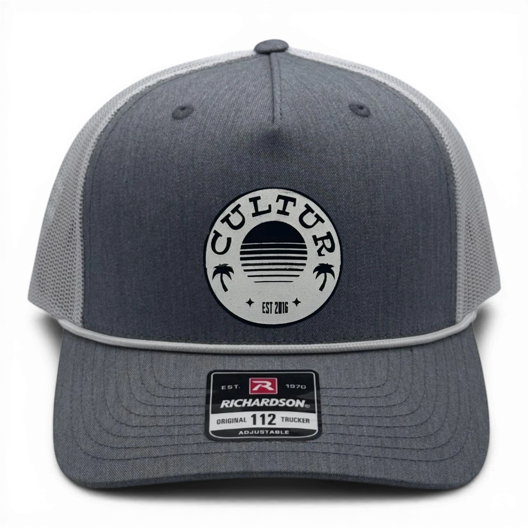 CULTUR grey trucker hat with white mesh back and circular CULTUR logo patch featuring a sunset and palm trees.