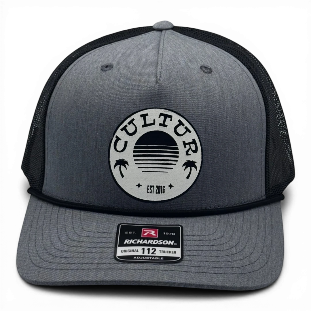 CULTUR grey trucker hat with black mesh back and circular patch featuring palm trees and a sunset.