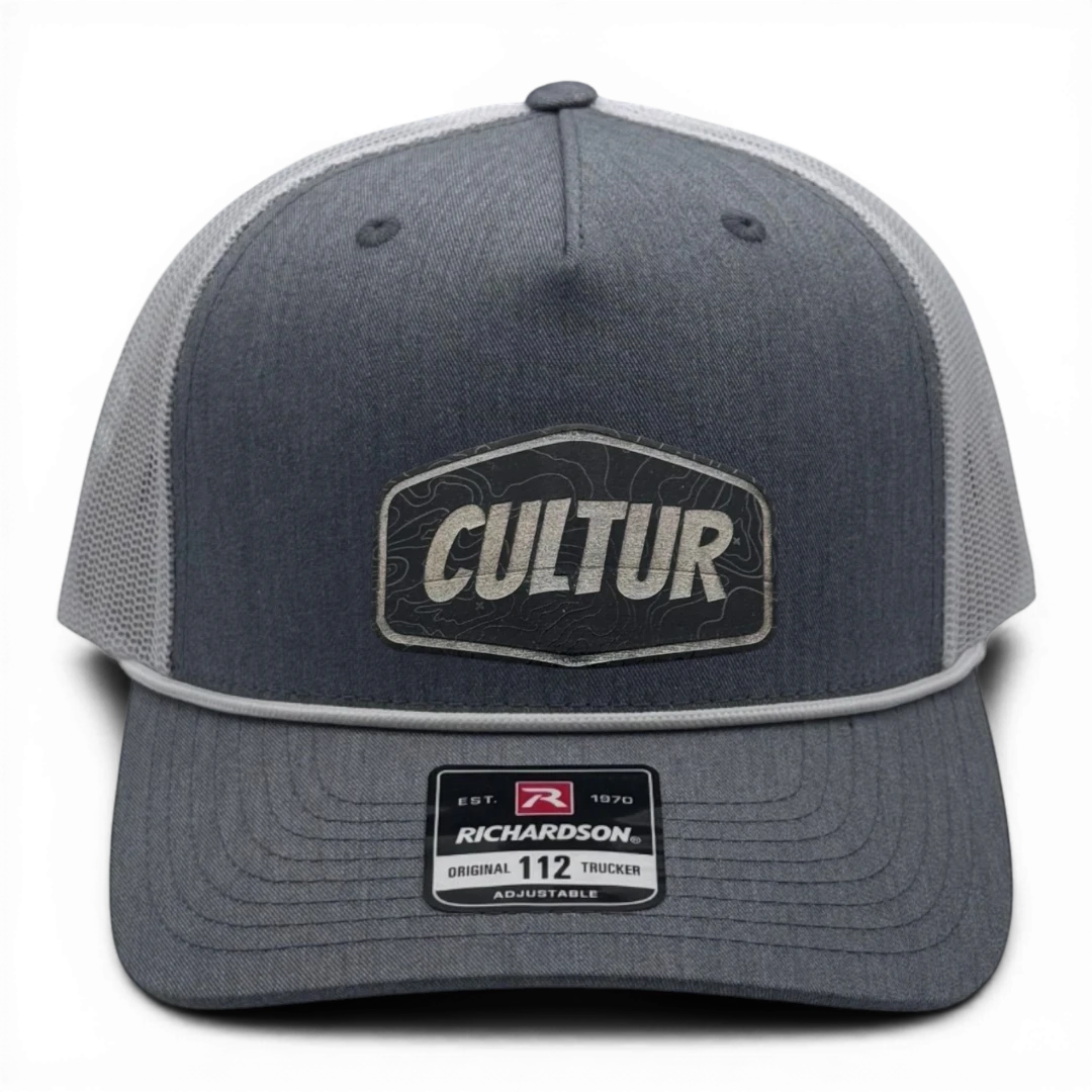 CULTUR Topo Trucker Hat in charcoal grey with a white mesh back and a CULTUR topographic patch.