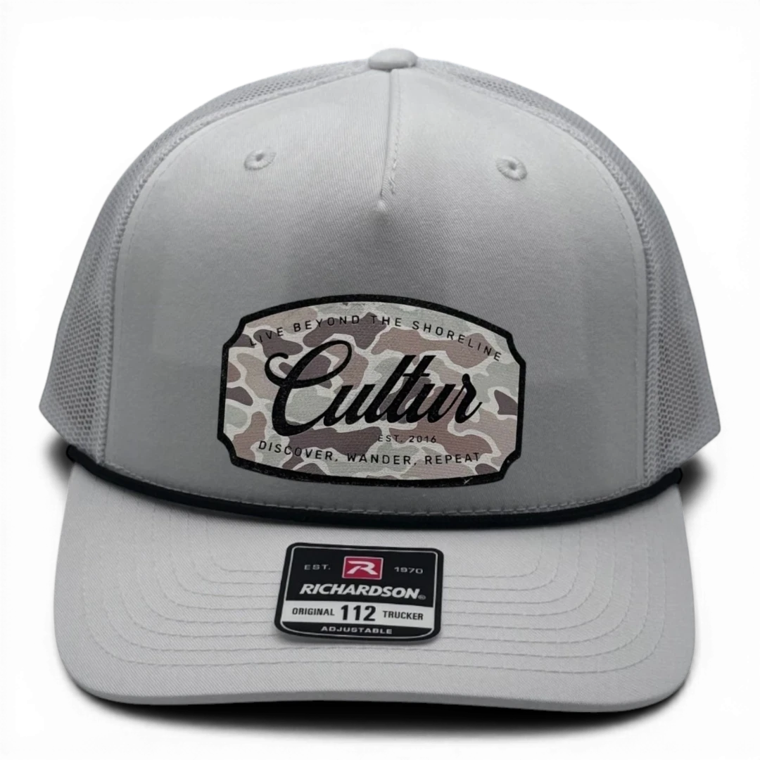 CULTUR white trucker hat with a camouflage patch featuring the CULTUR logo and text.