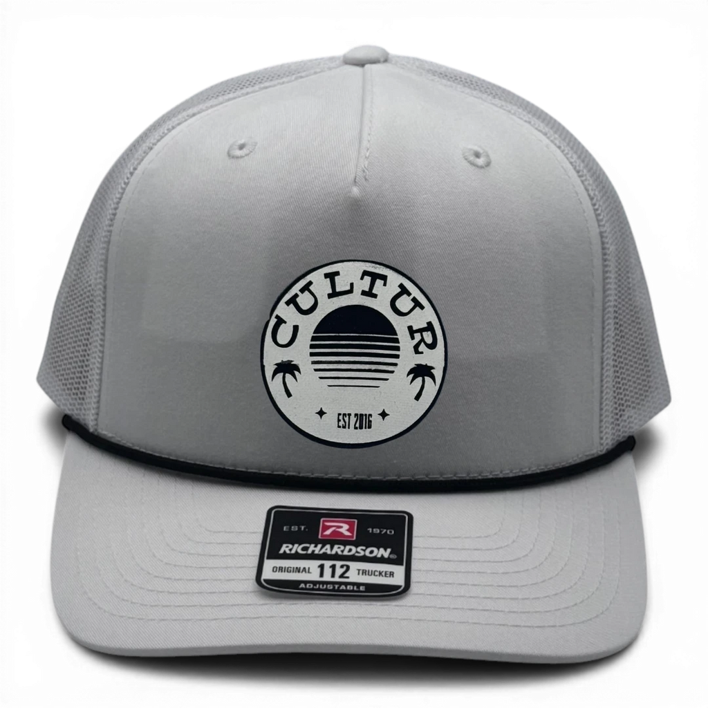 CULTUR white trucker hat with black rope, mesh back and circular patch featuring sun and palm trees.