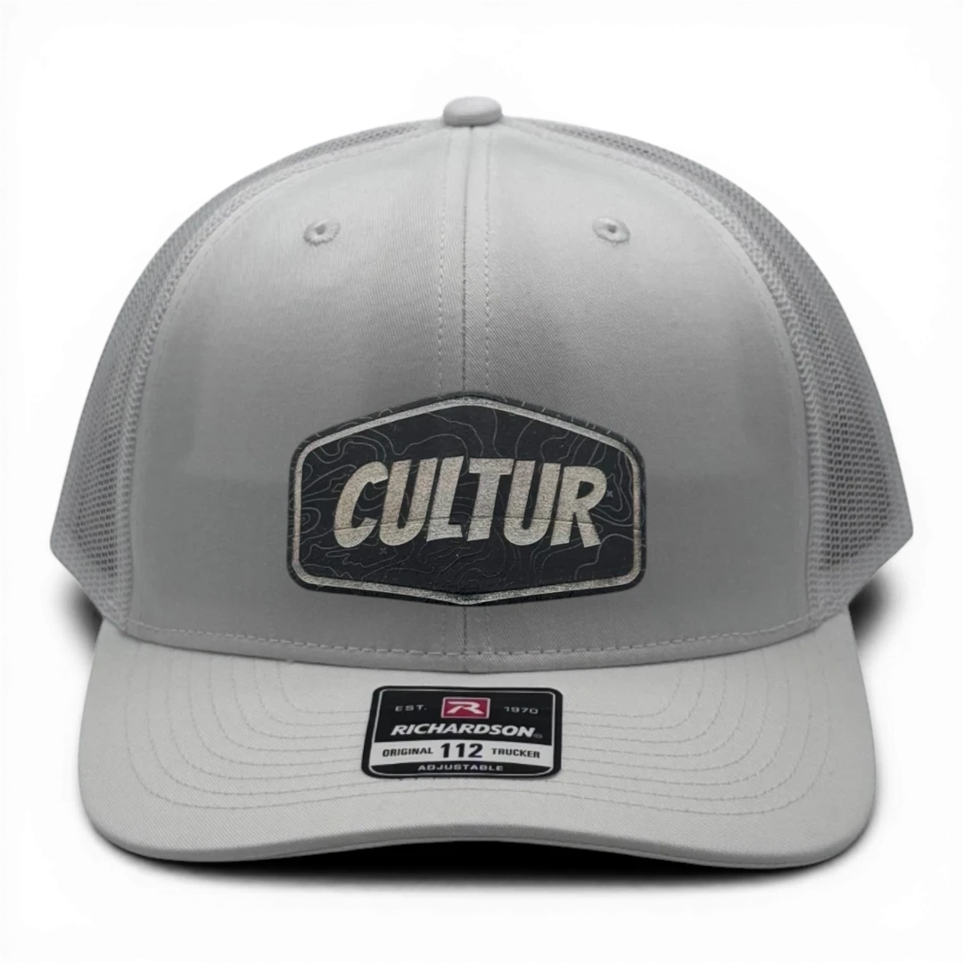 CULTUR white trucker hat with mesh back and embroidered CULTUR Topo patch design. Adjustable fit.