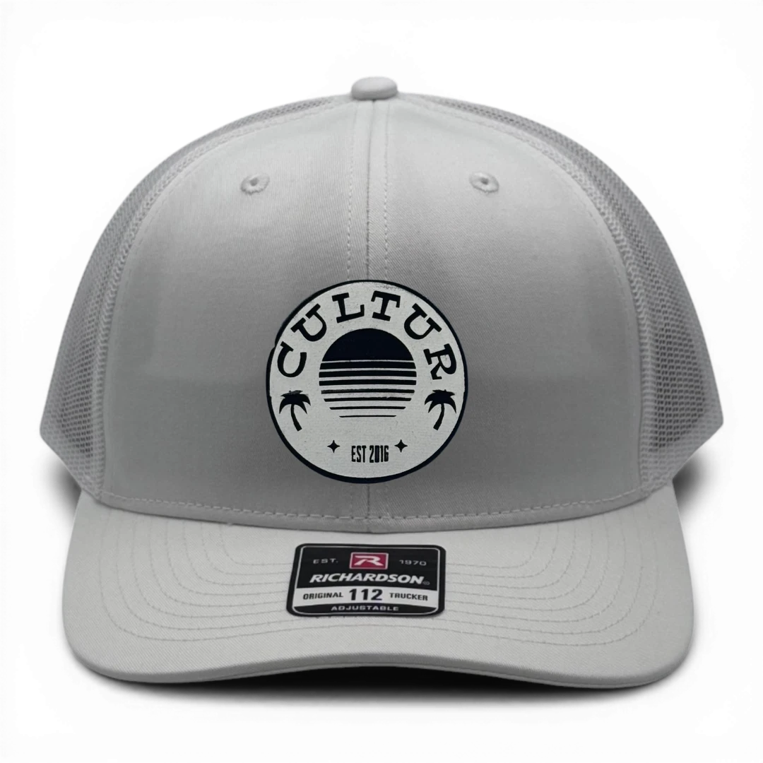 CULTUR white trucker hat with mesh back and circular logo featuring palm trees and a sunset.