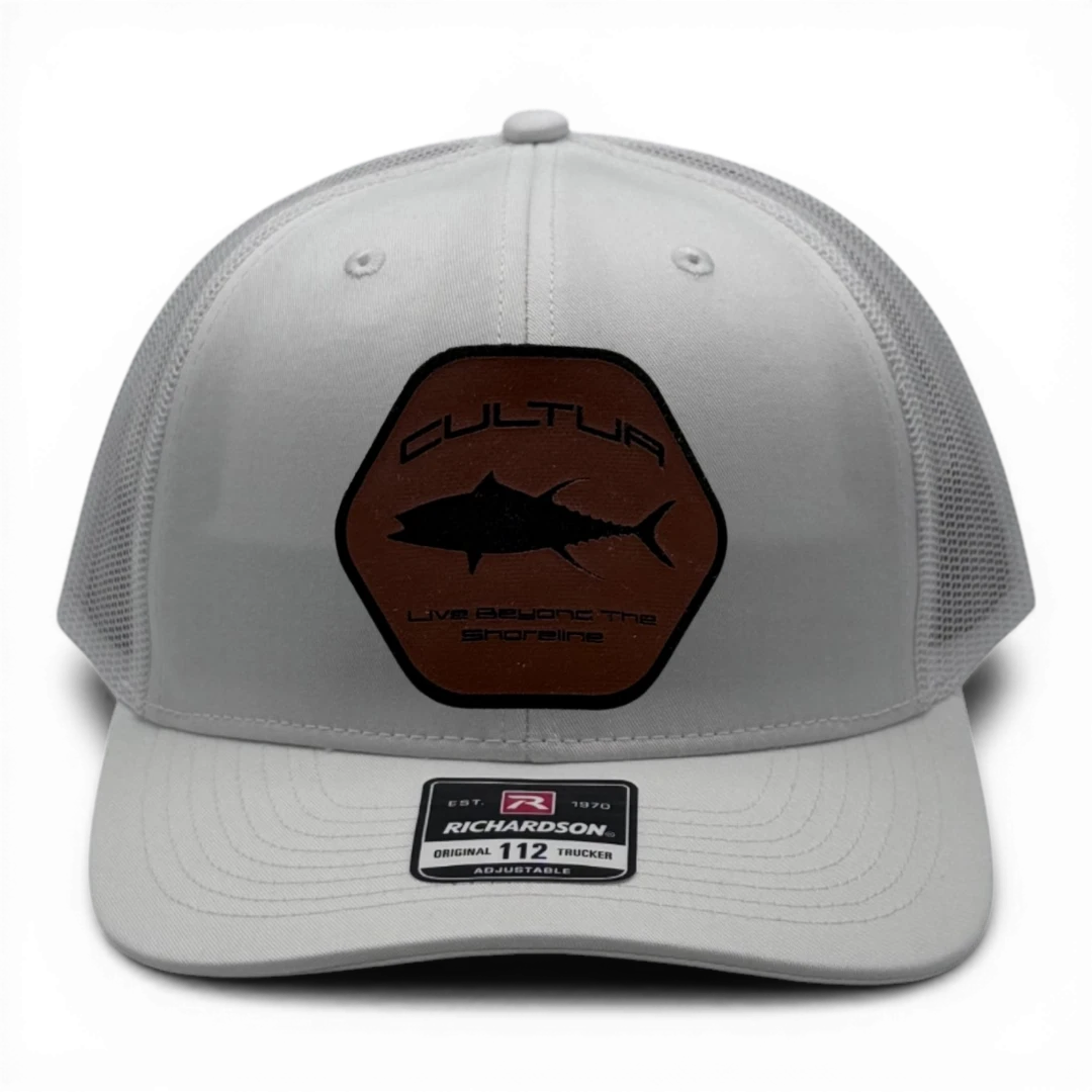 CULTUR white trucker hat with a hexagonal brown patch featuring a black tuna silhouette and the text "CULTUR Live Beyond The Shoreline".